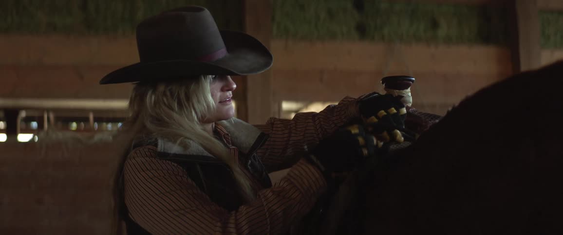 A woman taking a saddle off a horse in a barn