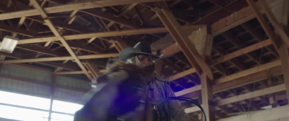 A woman sitting on a horse in a stable turns the horse in a different direction