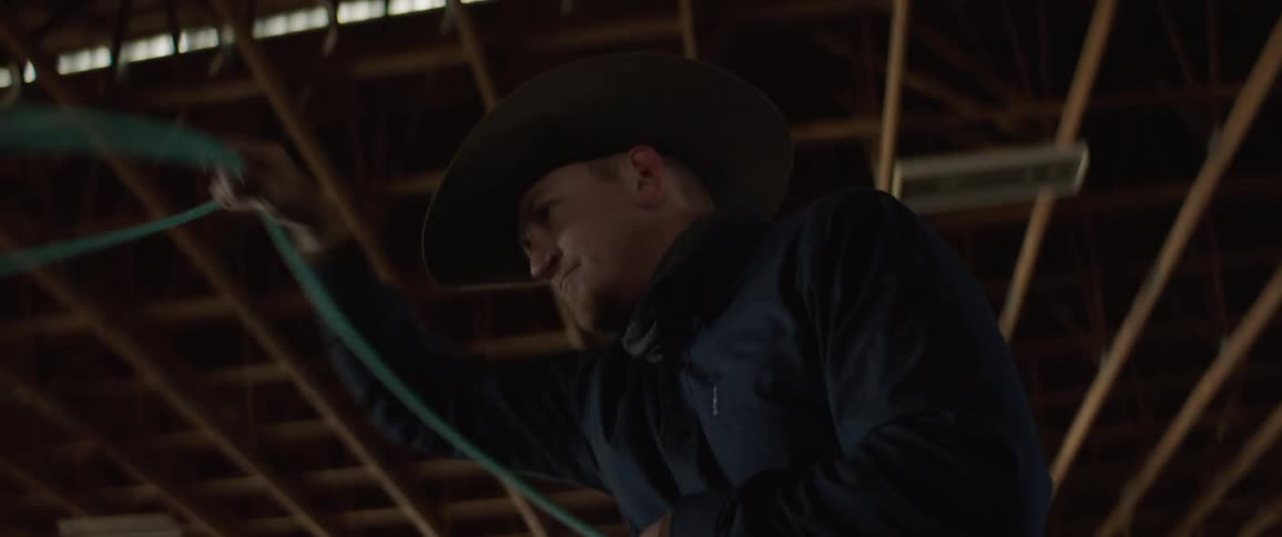 Cowboy spinning a lasso over his head inside a stable