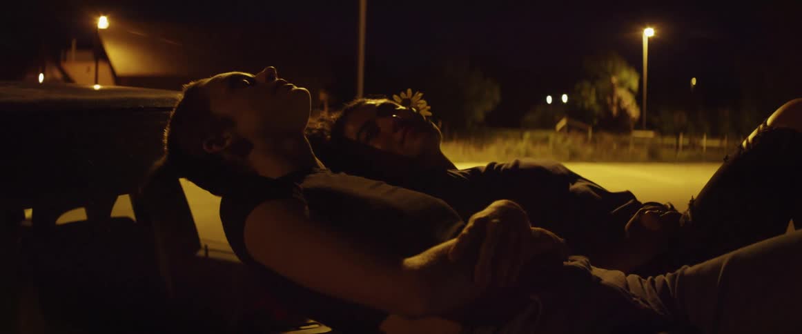 There are two people that are laying on a cars hood