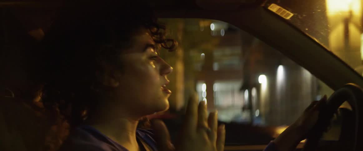 Young girl dancing while driving a car in the city at night