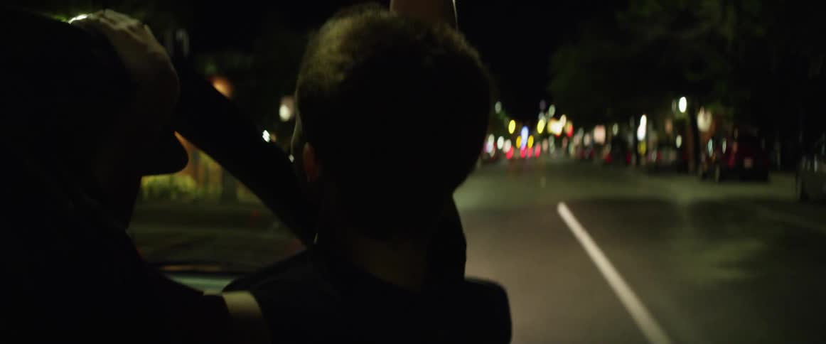 Young woman leaning out of window of moving car at night