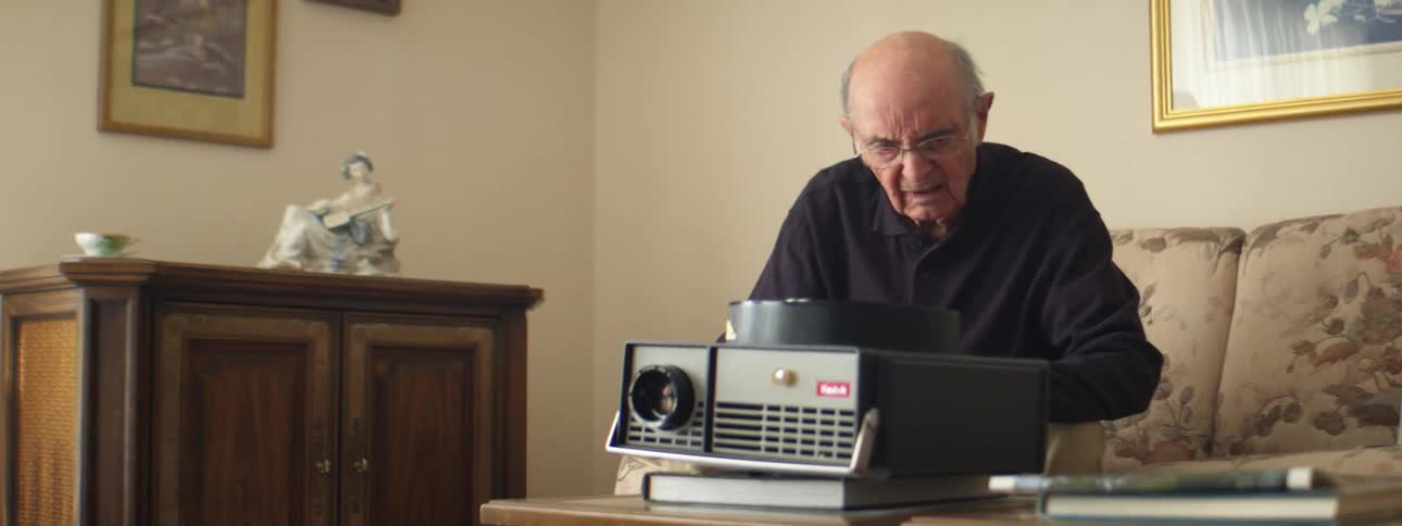 A man in a room sitting on a couch with a projector on a book on a table