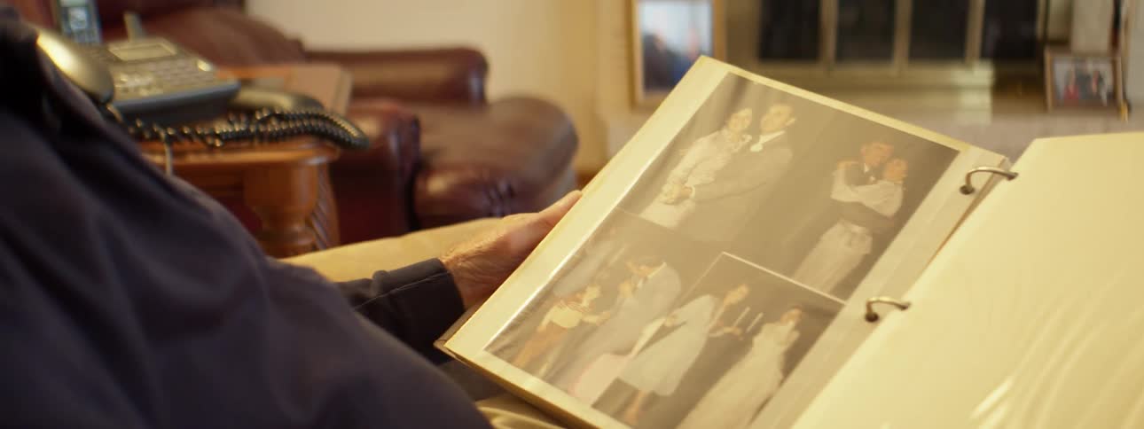A man sits at home and looks through a binder of photographs
