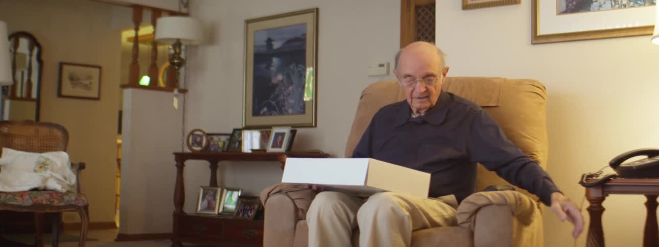 Elderly man sitting on a couch in the living room unwraps a present