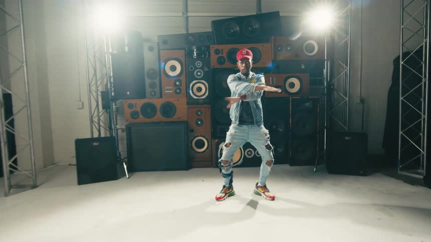 Man dressed in denim energetically dancing in front of a tower of speakers
