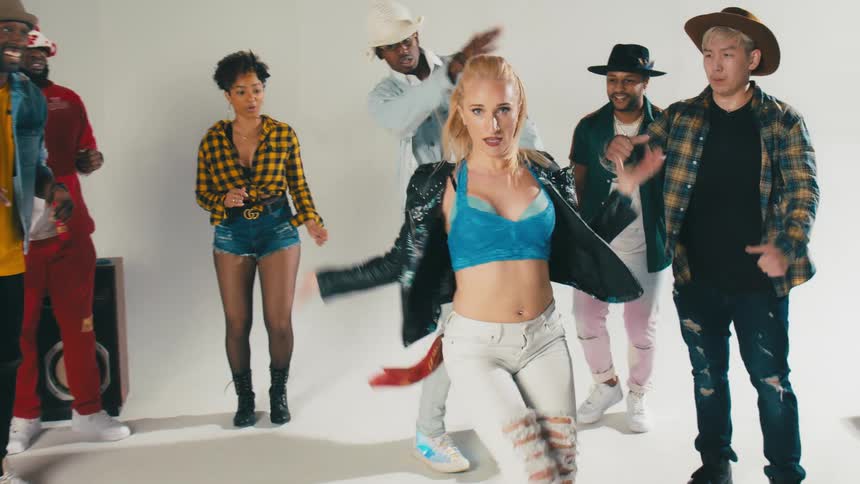 Women and men in a room dancing with a wall and speakers in the background