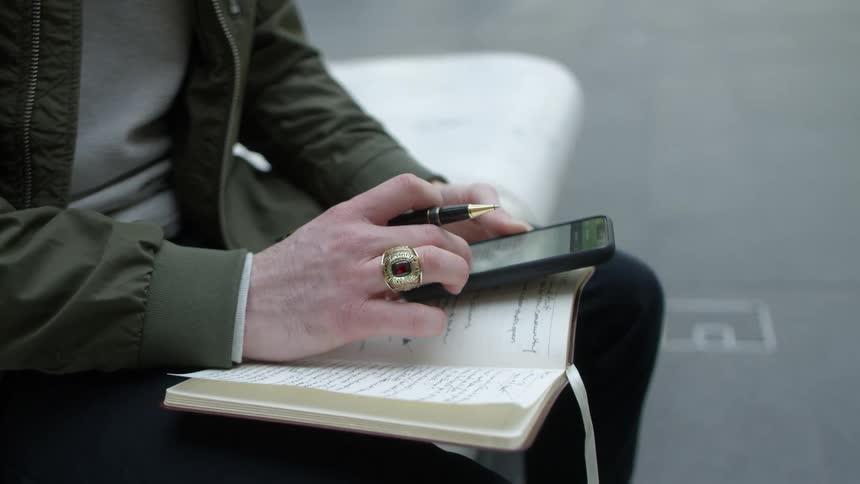 A person with a ring and a pen looking at a smart phone and holding a book