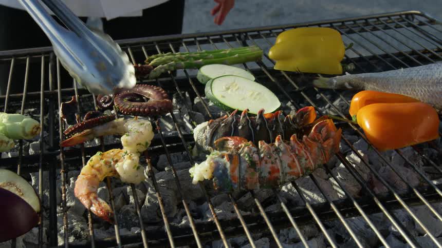 A chef flips over shrimp as he grills over charcoal outdoors