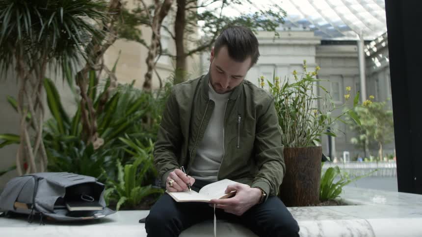 A man sits and writes in a notebook
