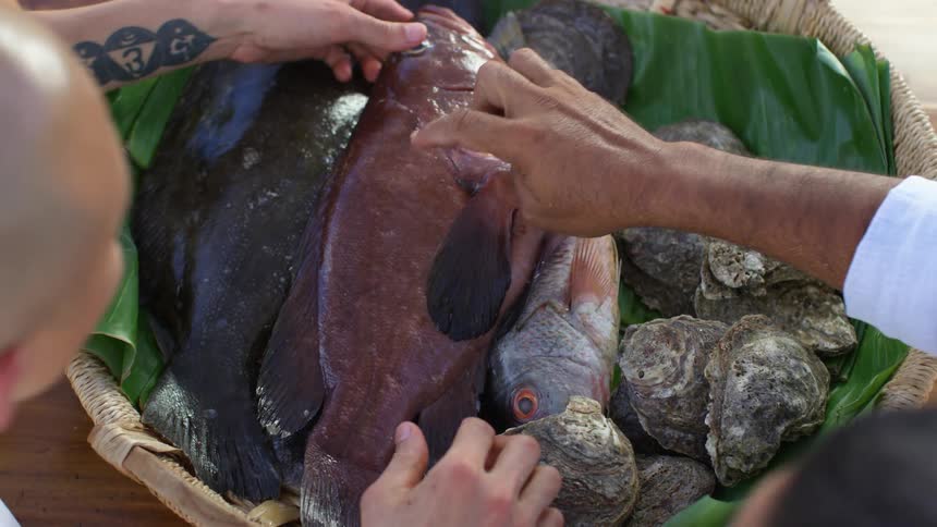 Two men look at fish in a basket