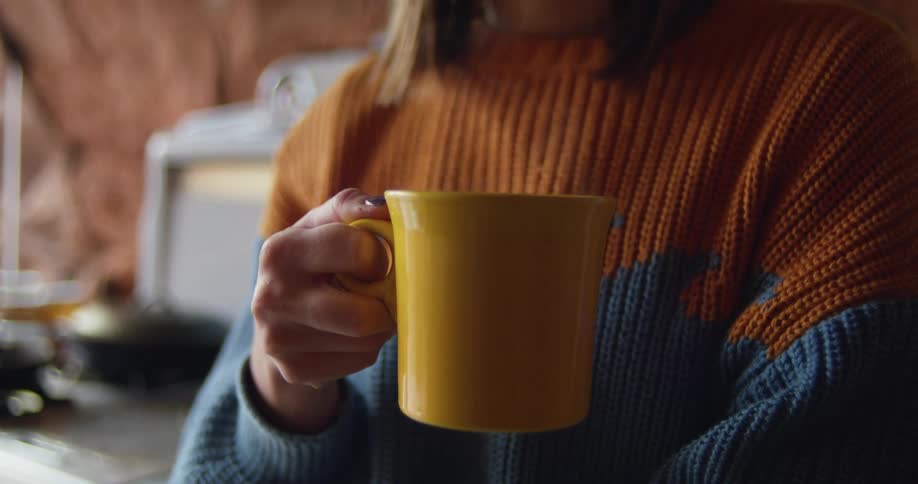 A woman holds a steaming beverage at home