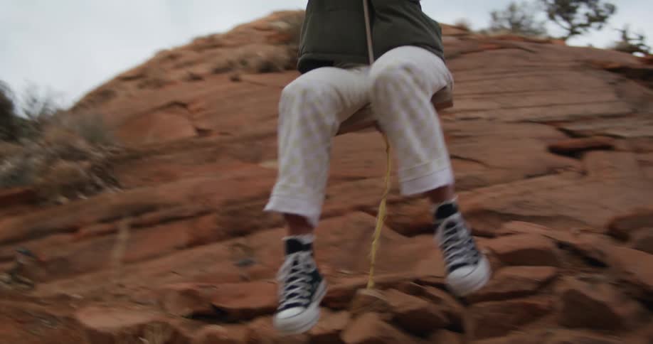 A woman swings on a tree rope swing pushing off the rock when she gets close to the cliff
