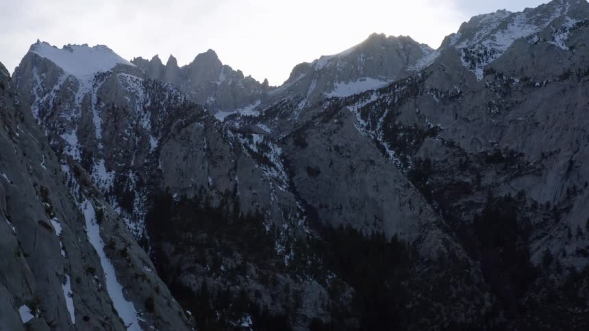 A mountain range with snow and ice with the sky and clouds in the background