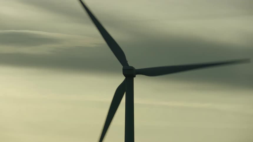 Tight aerial shot looking up at a wind turbine as it generates electricity with lenticular clouds in the background