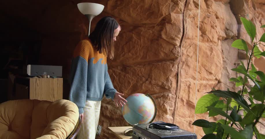 A teenage girl spins a globe in a living room