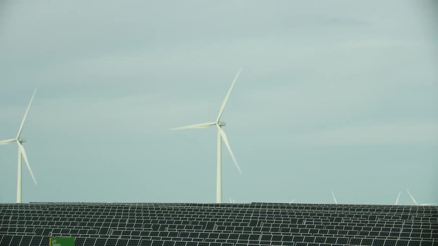 Static shot of wind turbines and solar panels in the same frame communicating the efficiency and power of renewable energy generation