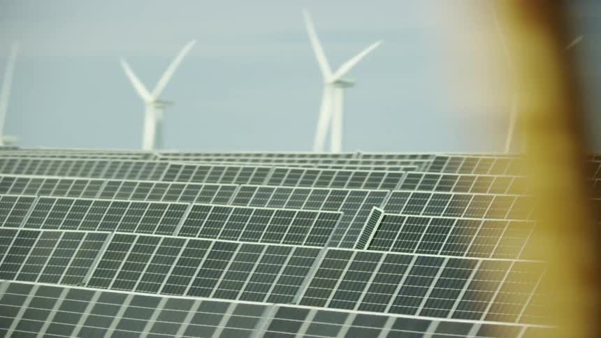 High energy and dynamic shot as the camera rapidly pans right to reveal row after row of solar panels and wind turbines in the same shot