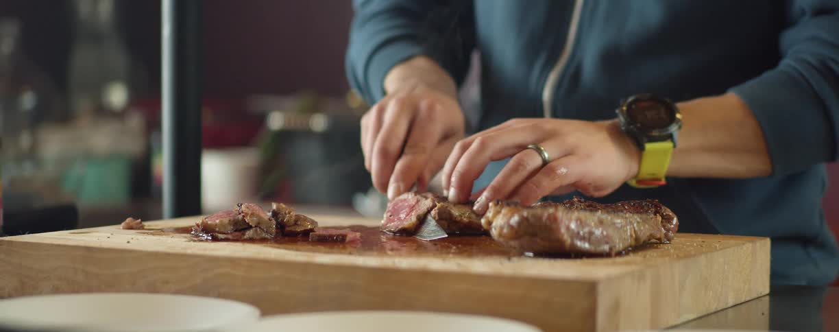 Person slices cooked meat sitting on wooden chopping board