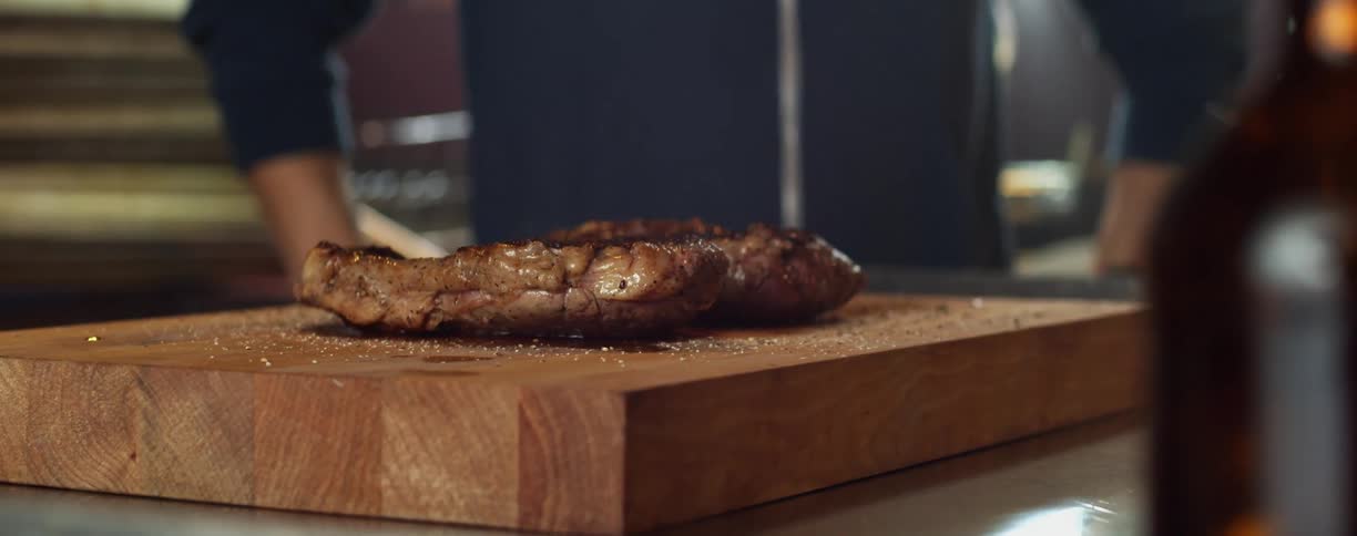 A person in a room standing with a piece of meat on a cutting board on a table