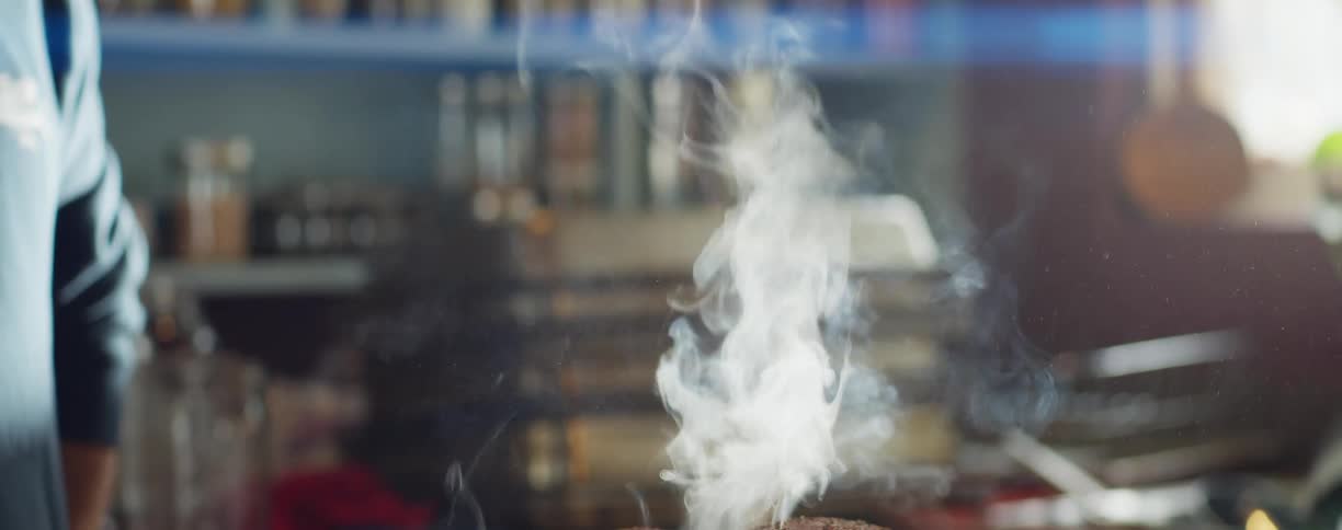 Smoke rises from two large steaks cooking in a black circle pan