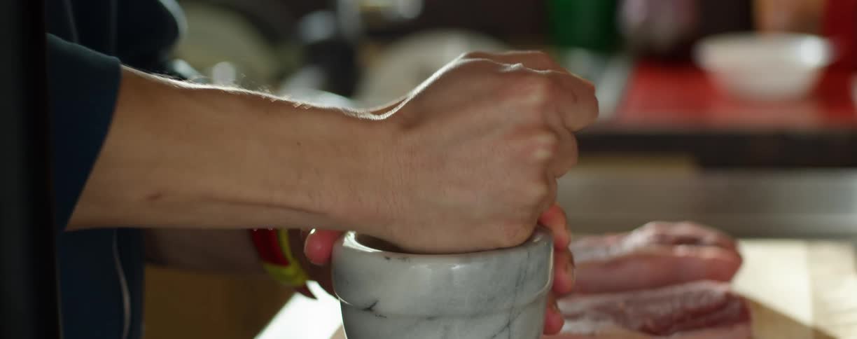 A man uses a mortar and pestle near a cutting board with meat on it