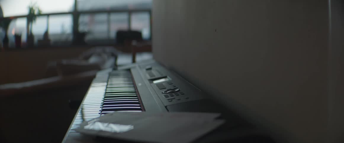 Mail sits on electric keyboard sitting next to wall in room with view of buildings