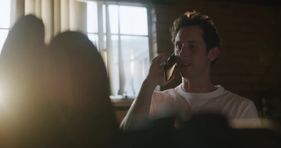 Man sitting at a desk at home talking on a smartphone at sunset