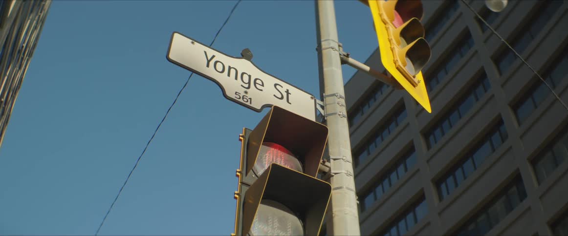 A pole with traffic lights and signs with a building and the sky above
