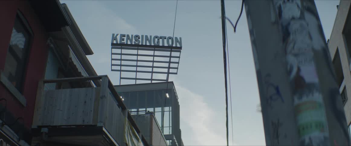 A large sign with a citys name sits above apartment buildings in a city