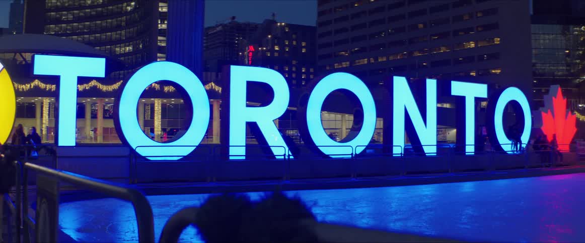 A large blue sign in a city at night time spells out the word toronto with a red maple leaf on the end
