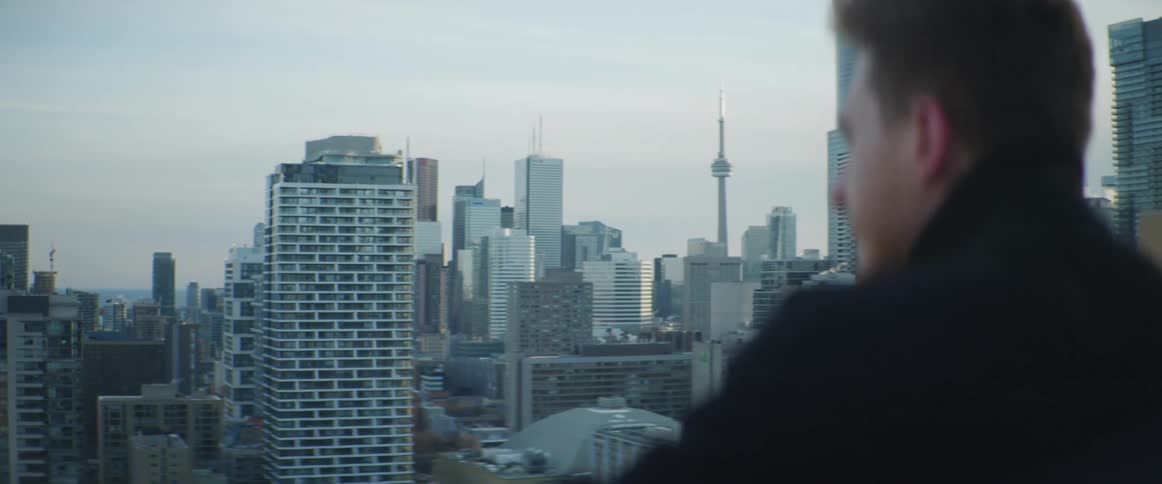 A man on a rooftop with a city skyline buildings the sky and clouds in the background