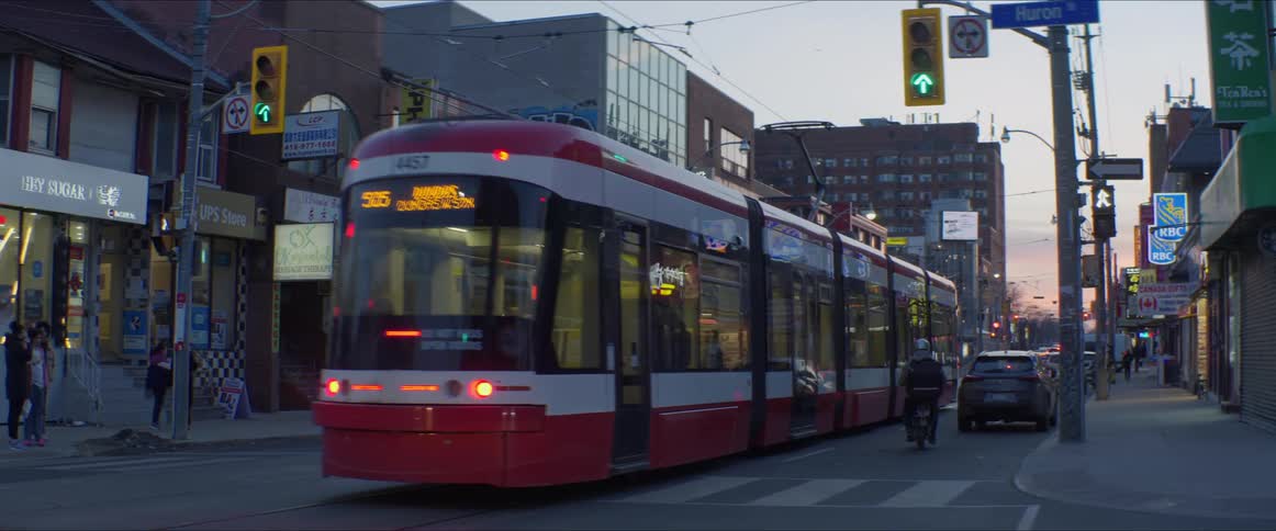 A light rail train travels down a city street at sunset