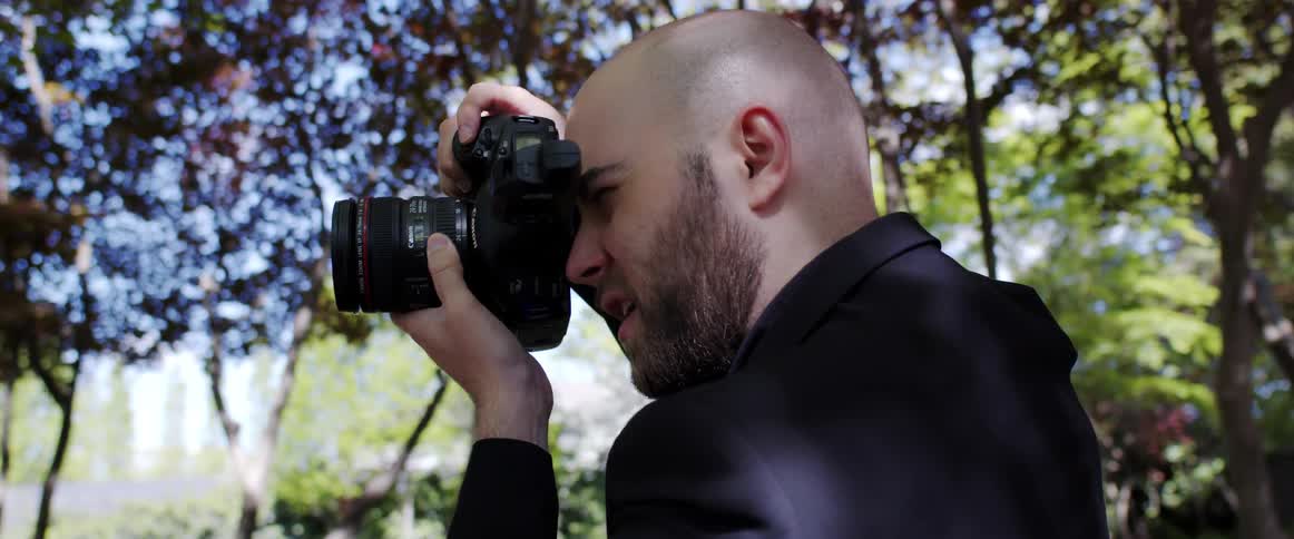 A man with a camera taking pictures with trees the sky and clouds in the background