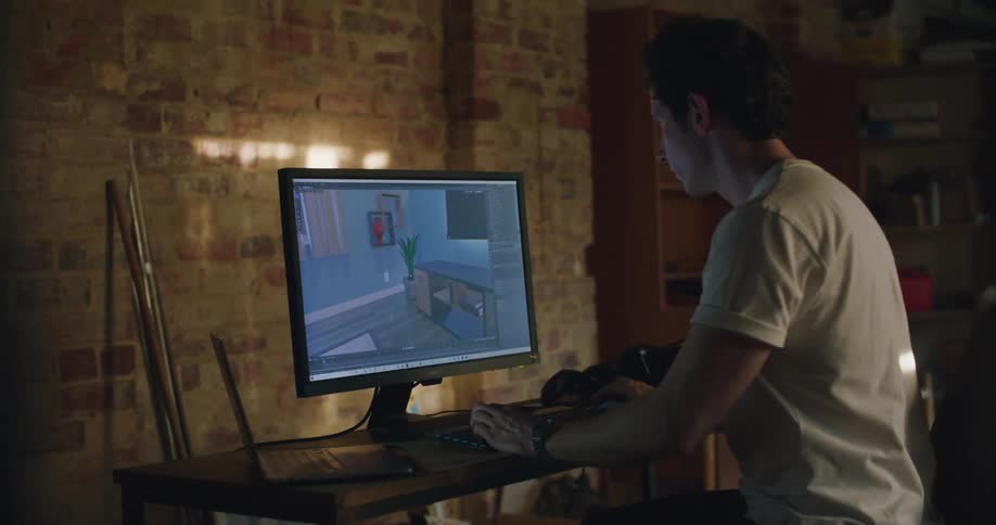 A man in a room sitting on a desk with a laptop and computer