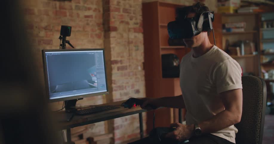 A man uses a virtual reality headset to inspect a 3D model while sitting at desk indoors