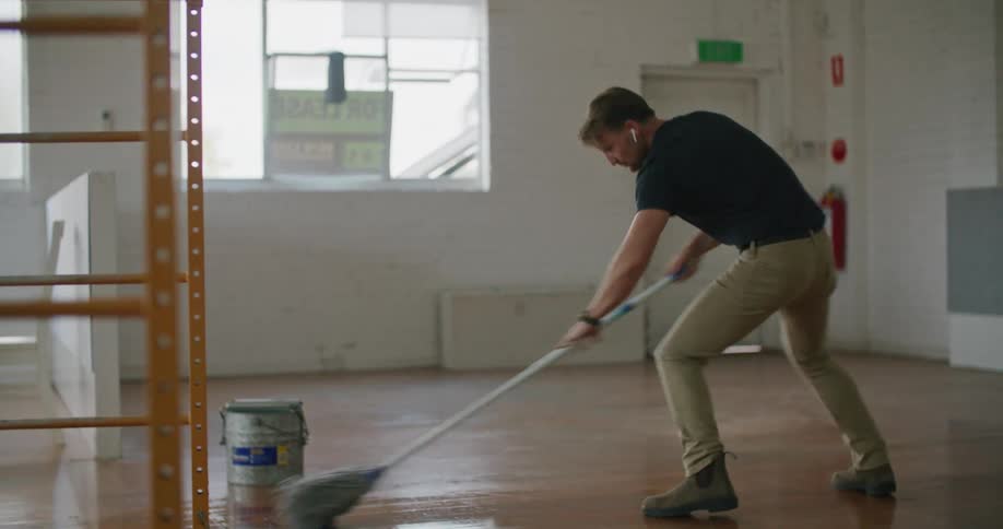 A man in a room mopping the floor with a mop and dancing with a wall and door in the background