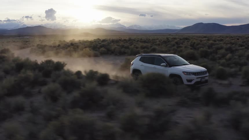 Sports utility vehicle drives along narrow dirt track through scrub kicking up dust with misty mountains on the horizon
