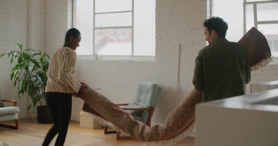 A man and woman carrying a rug into a house