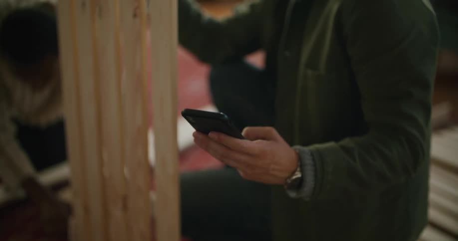 A man and a woman in a room putting together furniture with a man looking at a smart phone