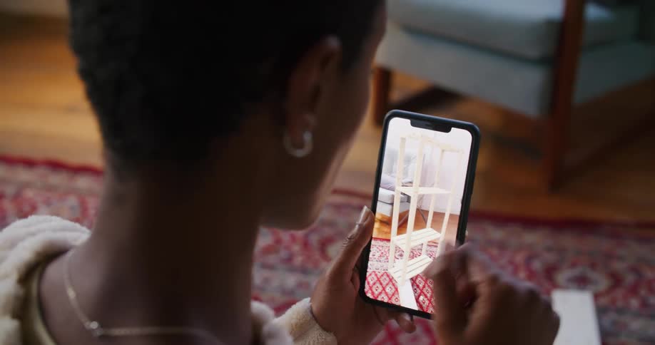 A woman with a necklace in a room looking at a smart phone with a chair in the background