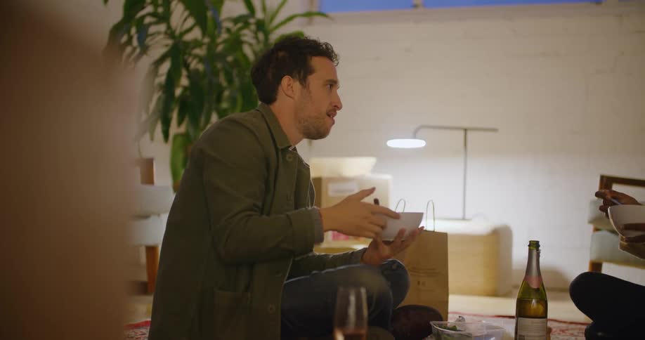 Man sits on floor with friend talking while eating
