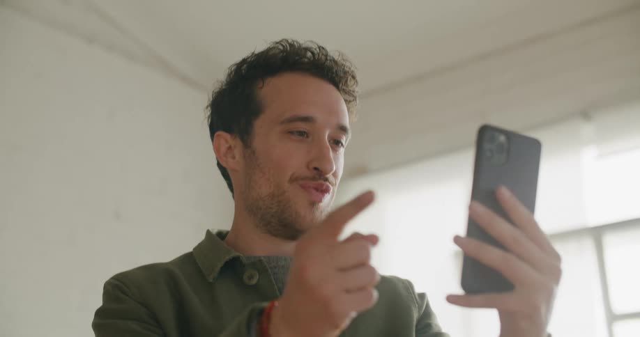 A man in a room looking at a smart phone with a wall and window in the background