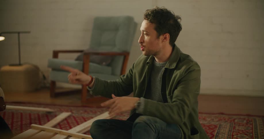 A man and a woman on the floor putting together furniture with a plant and walls in the background