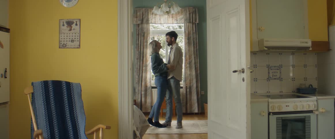 A man and woman hug and kiss in a room access through a kitchen door