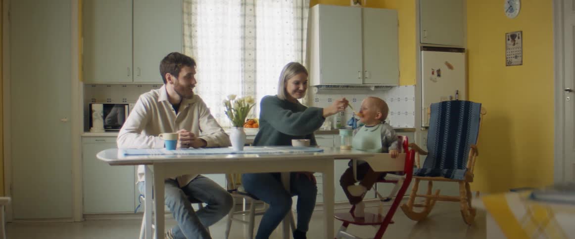 Family dressed in long sleeves sits at kitchen table while mother feeds boy sitting in highchair