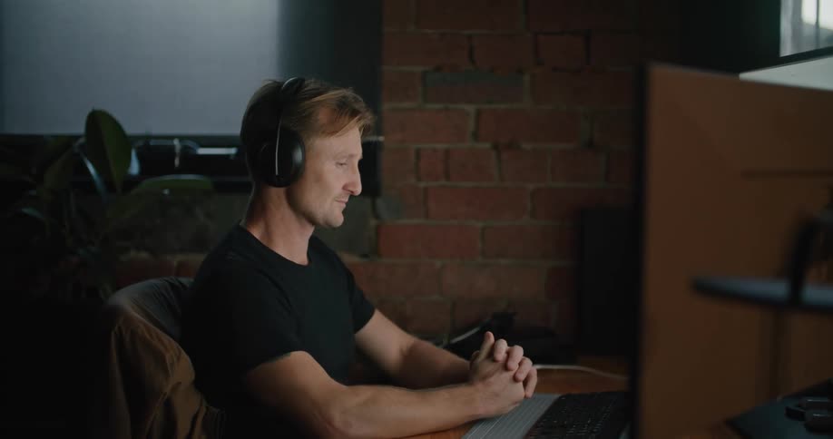 A man sitting at a desk stretches his neck while typing on a computer keyboard indoors during the day