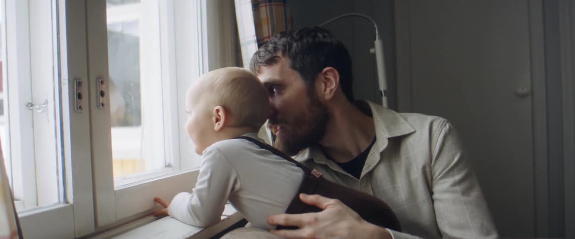Man holds son securely as they talk and look out window