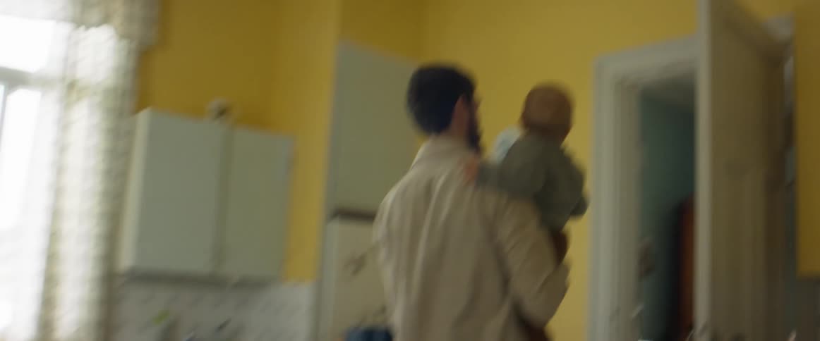 A dad jogs through the house carrying his son turning around when they get to mom