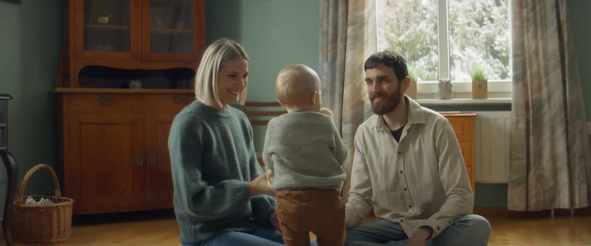 Parents and toddler play with teddy bear in living room